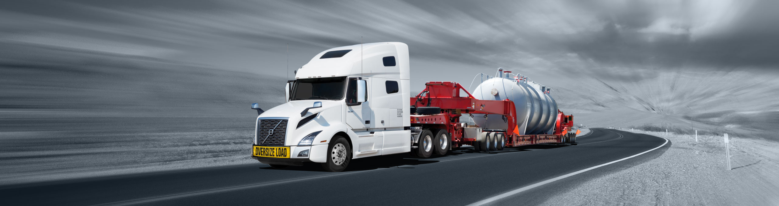 Truck hauling large piece of equipment with specialized drop deck trailer